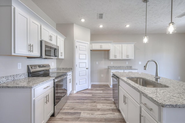 kitchen featuring light wood-style floors, a center island with sink, white cabinets, a sink, and stainless steel appliances
