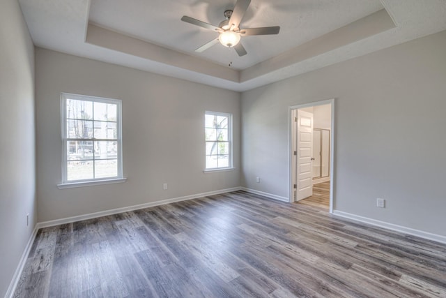 spare room featuring baseboards, a tray ceiling, ceiling fan, and wood finished floors