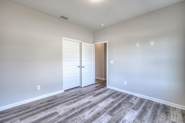unfurnished bedroom with visible vents, a textured ceiling, baseboards, and wood finished floors