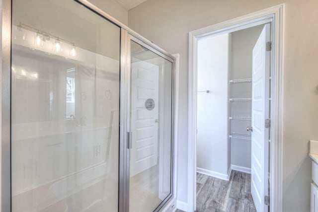 bathroom with a walk in closet, a stall shower, wood finished floors, vanity, and baseboards
