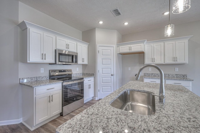 kitchen with white cabinets, a sink, stainless steel appliances, wood finished floors, and visible vents