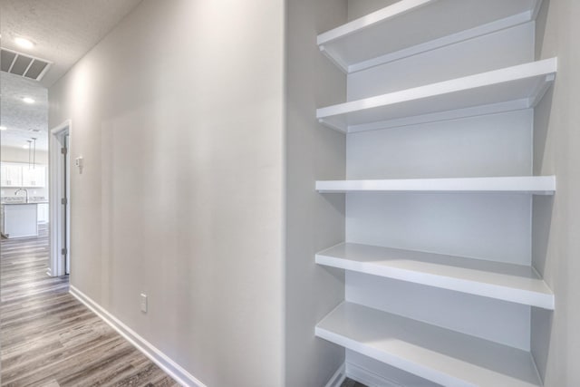 hall with a sink, a textured ceiling, baseboards, wood finished floors, and visible vents