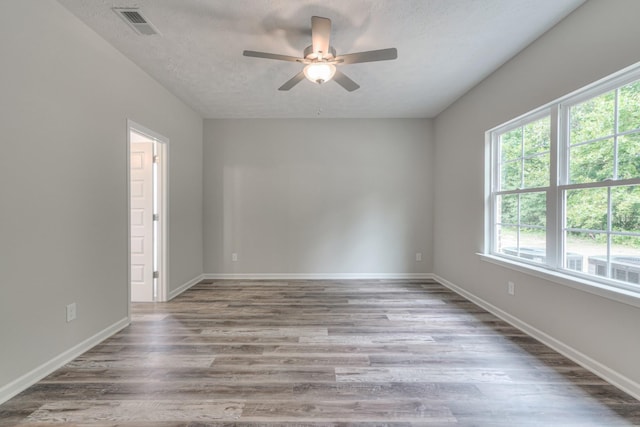 empty room featuring visible vents, wood finished floors, baseboards, ceiling fan, and a textured ceiling
