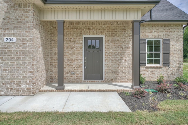 view of exterior entry with brick siding and a shingled roof