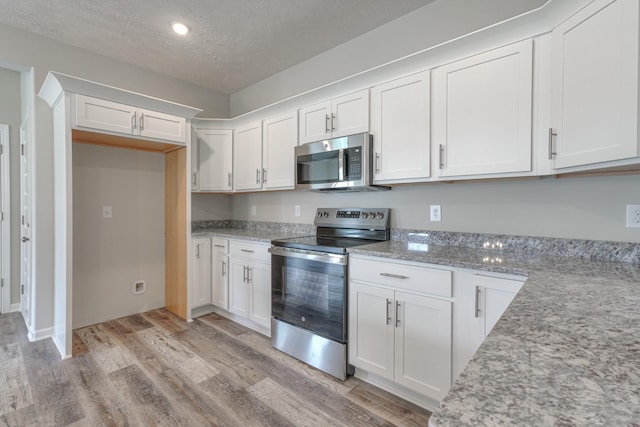 kitchen with stainless steel appliances, a textured ceiling, white cabinetry, and light wood-type flooring