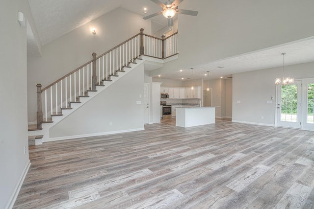 unfurnished living room featuring stairway, high vaulted ceiling, baseboards, ceiling fan with notable chandelier, and light wood-style floors
