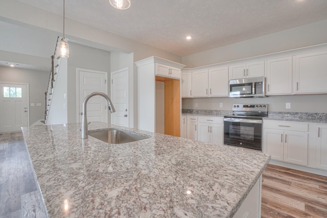 kitchen featuring light stone countertops, an island with sink, white cabinetry, a sink, and appliances with stainless steel finishes