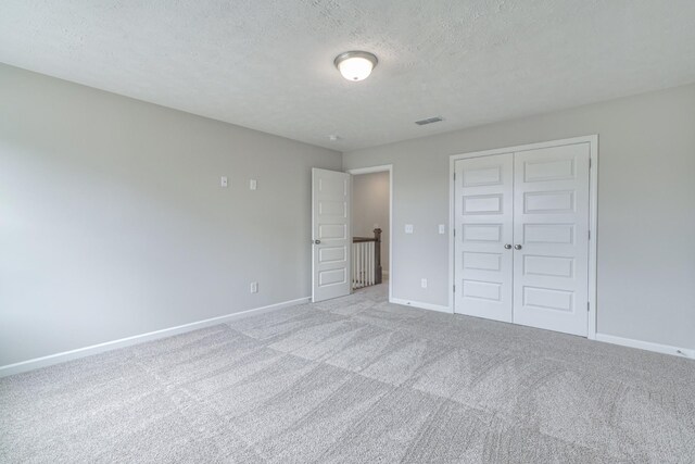 unfurnished bedroom with a textured ceiling, visible vents, carpet floors, baseboards, and a closet