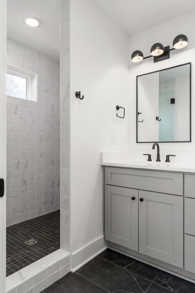 full bath featuring baseboards, a tile shower, marble finish floor, and vanity
