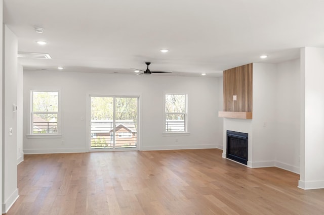 unfurnished living room featuring a ceiling fan, light wood finished floors, a wealth of natural light, and a large fireplace