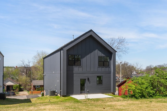 rear view of house featuring a lawn, central AC unit, board and batten siding, and a patio area