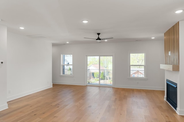 unfurnished living room with baseboards, a fireplace, a ceiling fan, and light wood-type flooring