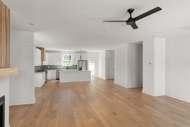 unfurnished living room with a ceiling fan, baseboards, a sink, and light wood-type flooring