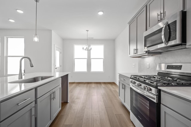kitchen featuring gray cabinets, appliances with stainless steel finishes, a sink, light countertops, and a notable chandelier