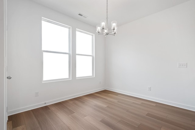empty room featuring visible vents, baseboards, wood finished floors, and a notable chandelier
