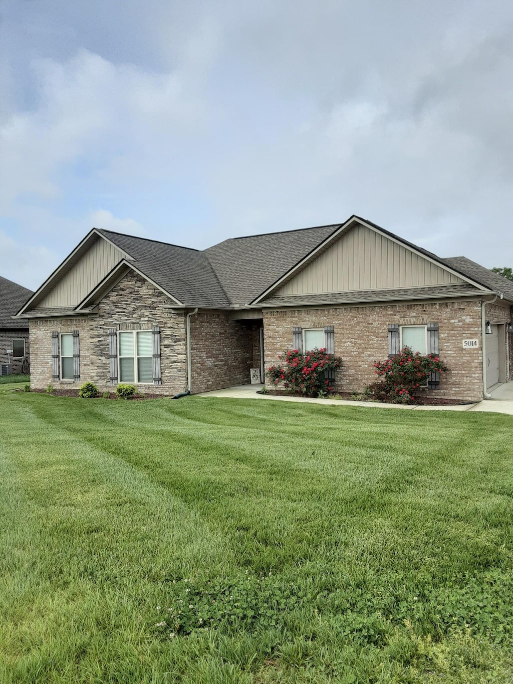 view of front facade with brick siding, roof with shingles, and a front lawn