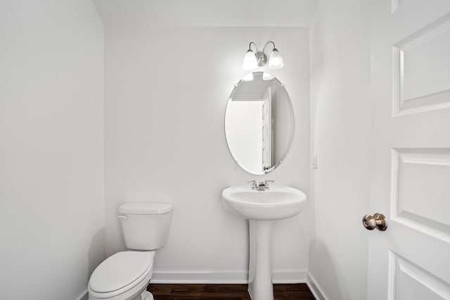 half bathroom with baseboards, toilet, and wood finished floors