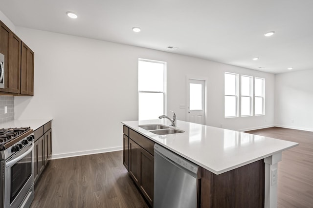 kitchen featuring backsplash, appliances with stainless steel finishes, a sink, light countertops, and dark wood-type flooring