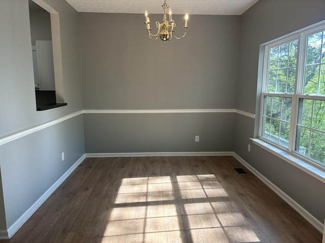 empty room featuring visible vents, baseboards, an inviting chandelier, and hardwood / wood-style flooring