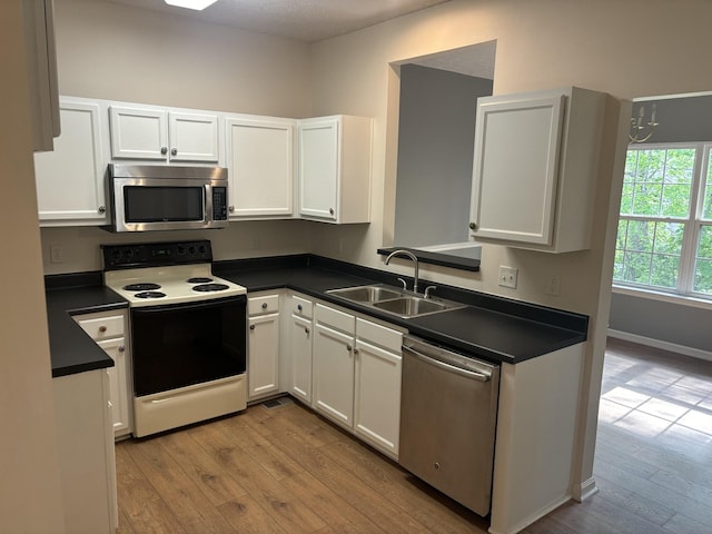 kitchen featuring wood finished floors, dark countertops, white cabinetry, a sink, and appliances with stainless steel finishes