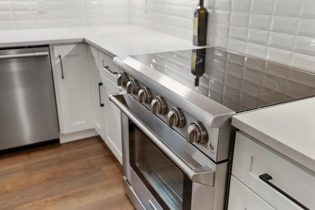room details featuring white cabinets, appliances with stainless steel finishes, light countertops, decorative backsplash, and wood finished floors