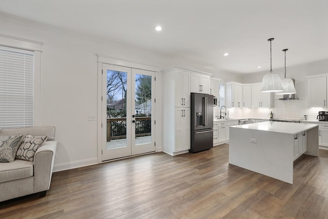 kitchen with wall chimney range hood, light countertops, french doors, a sink, and black appliances