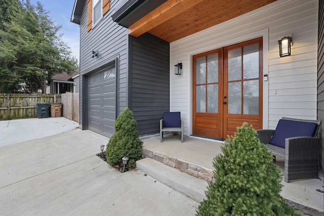 doorway to property featuring concrete driveway, fence, french doors, and a garage