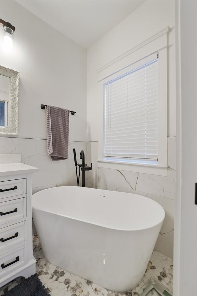 bathroom with tile walls, a soaking tub, vanity, and marble finish floor