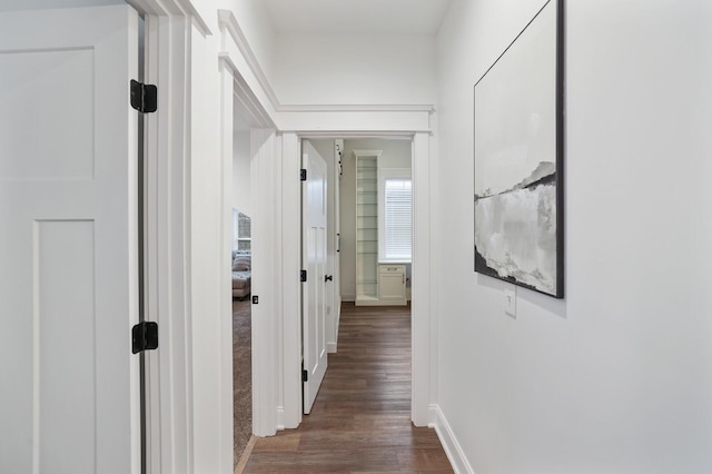 corridor featuring baseboards and dark wood-type flooring