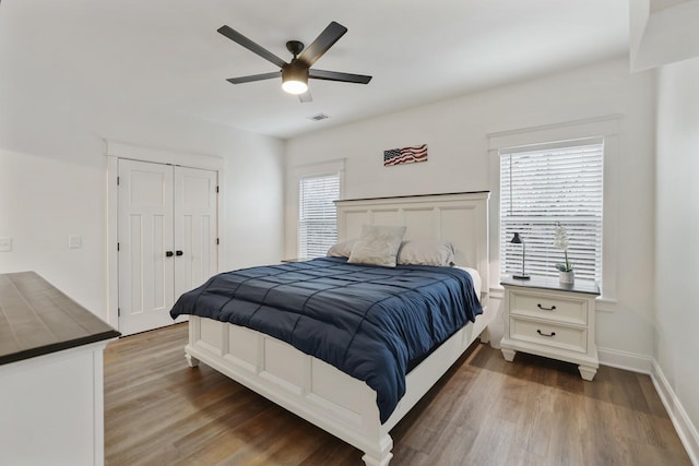 bedroom featuring ceiling fan, baseboards, wood finished floors, visible vents, and a closet