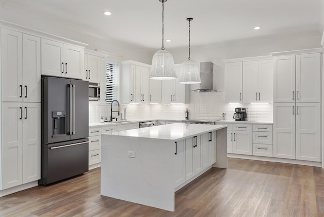 kitchen featuring appliances with stainless steel finishes, tasteful backsplash, a sink, white cabinets, and wall chimney exhaust hood