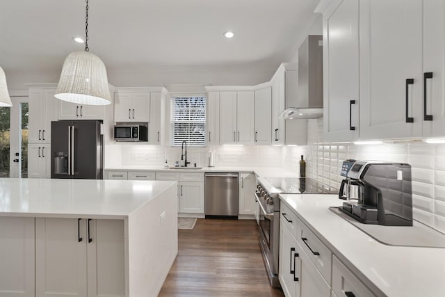kitchen with wall chimney range hood, high quality appliances, white cabinets, a sink, and backsplash