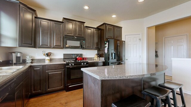 kitchen featuring dark brown cabinets, a breakfast bar, a center island, recessed lighting, and black appliances