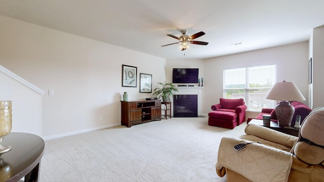 living area featuring a ceiling fan, visible vents, carpet floors, baseboards, and a glass covered fireplace
