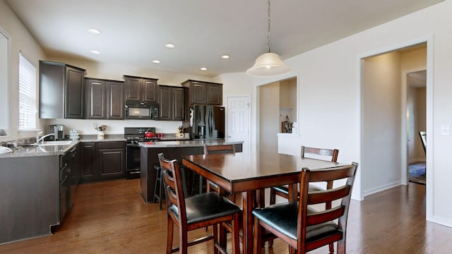 kitchen featuring a center island, dark brown cabinets, light countertops, black appliances, and dark wood-style floors