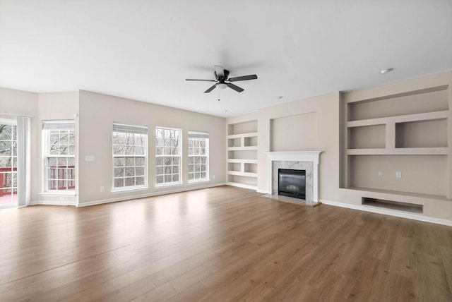 unfurnished living room with ceiling fan, built in features, wood finished floors, and a high end fireplace