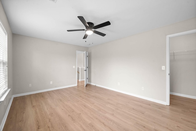 unfurnished bedroom featuring a closet, baseboards, ceiling fan, light wood-type flooring, and a spacious closet