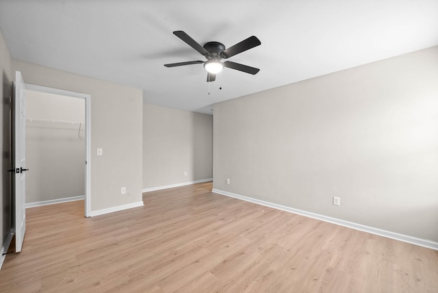 unfurnished bedroom featuring a ceiling fan, baseboards, a closet, light wood finished floors, and a spacious closet