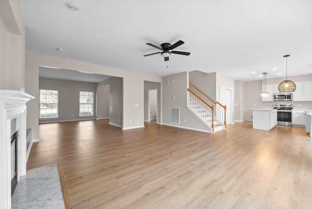 unfurnished living room featuring a ceiling fan, light wood-style flooring, a fireplace with flush hearth, and stairway