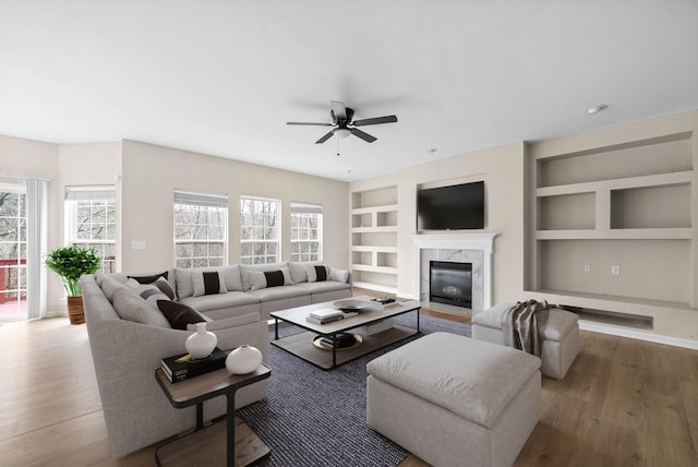 living room with a fireplace, built in shelves, a ceiling fan, baseboards, and wood finished floors