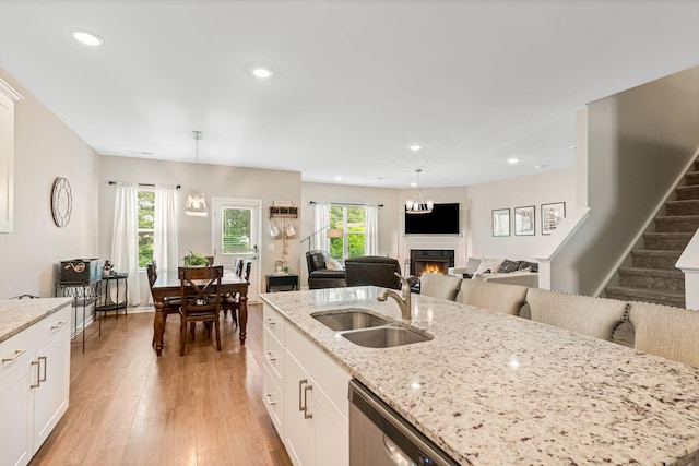 kitchen with hanging light fixtures, a sink, white cabinets, light wood-style floors, and a warm lit fireplace