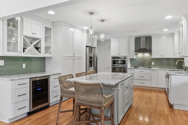 kitchen featuring a kitchen island, beverage cooler, a kitchen bar, wall chimney exhaust hood, and appliances with stainless steel finishes