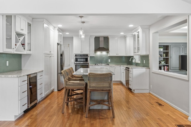 kitchen featuring decorative backsplash, beverage cooler, wall chimney exhaust hood, white cabinetry, and appliances with stainless steel finishes