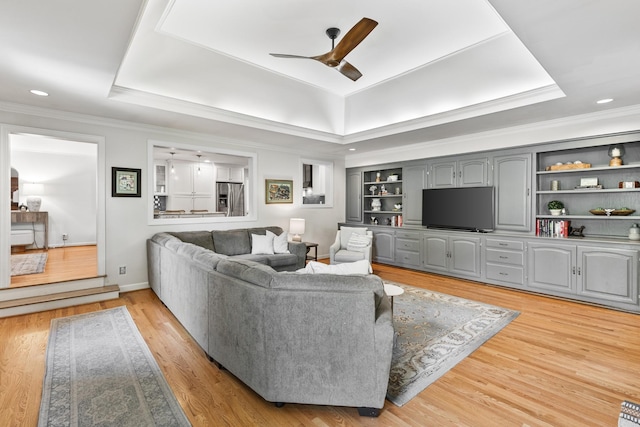 living area with crown molding, light wood-style flooring, a ceiling fan, baseboards, and a tray ceiling