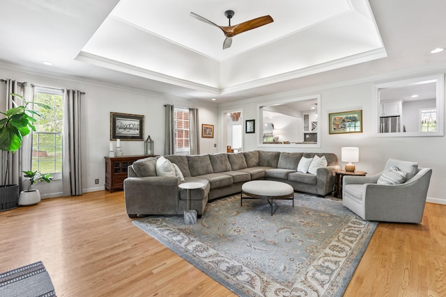 living area featuring a ceiling fan, a tray ceiling, a wealth of natural light, and light wood-style floors