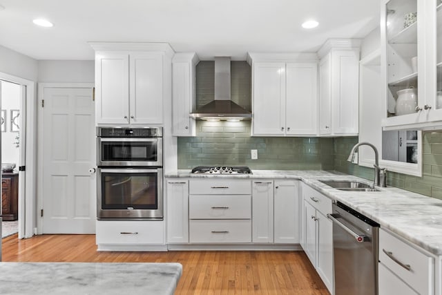 kitchen with wall chimney range hood, stainless steel appliances, white cabinetry, and a sink