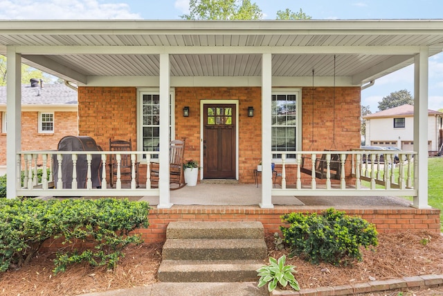 view of exterior entry featuring covered porch and brick siding