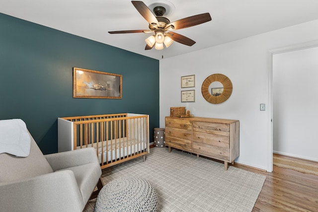 bedroom featuring a crib, baseboards, a ceiling fan, and wood finished floors