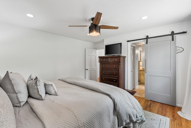 bedroom with recessed lighting, ceiling fan, a barn door, and light wood-style floors