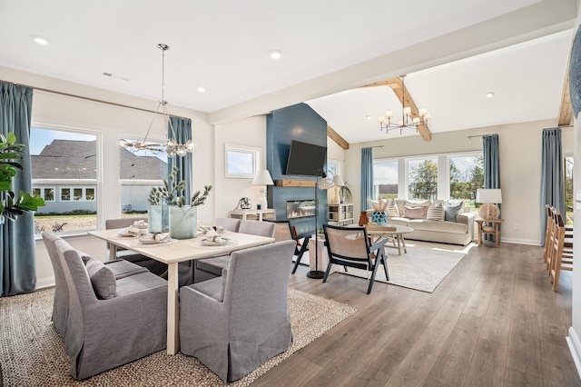 dining room with an inviting chandelier, a glass covered fireplace, vaulted ceiling with beams, wood finished floors, and visible vents